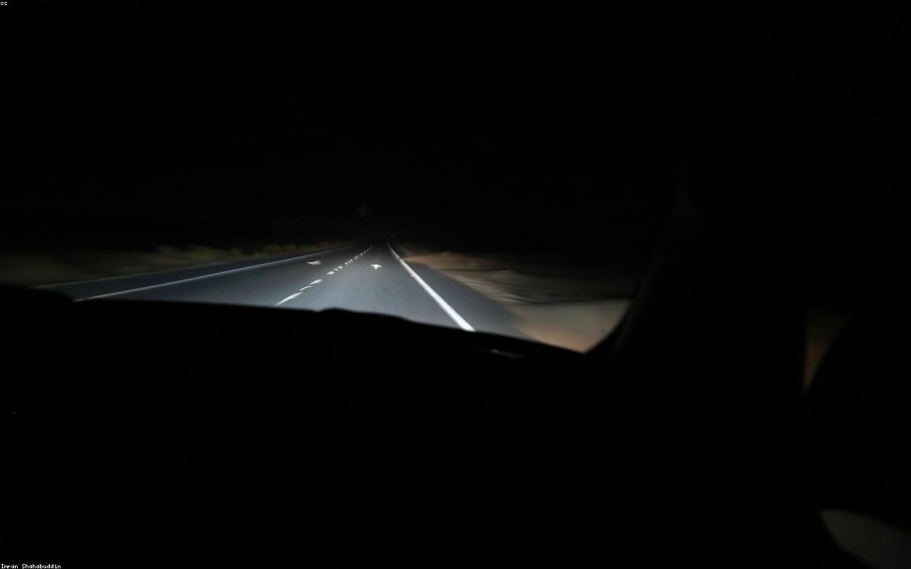 A driver's view of a dark highway at night, lane markings lit by headlights